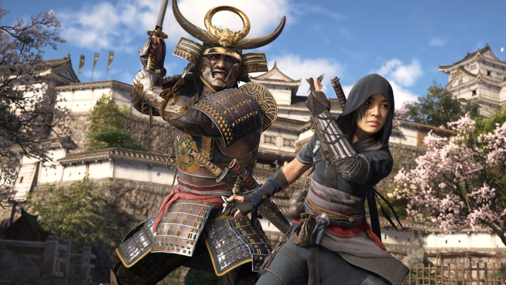 Assassin's Creed Shadows protagonists, Yasuke, a samurai in full armor with a horned helmet, stands ready with his katana, while Naoe, a shinobi in a dark, hooded outfit, crouches beside him with a blade, against a backdrop of a Japanese castle and cherry blossoms.
