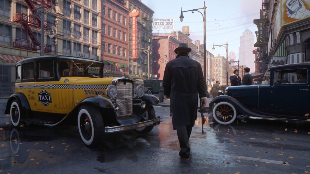 Tommy Angelo from Mafia: Definitive Edition walking down a wet 1930s Lost Heaven street, with a classic yellow taxi to his left and Prohibition-era buildings in the background.