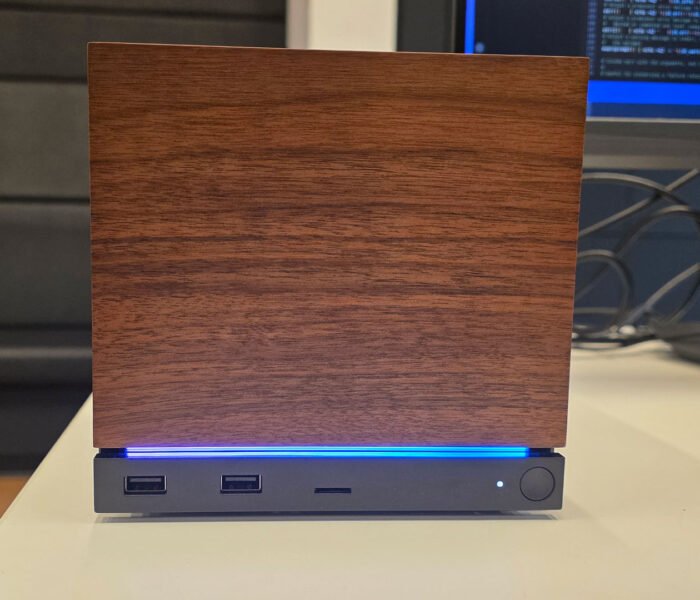 Steam Machine prototype sitting on a desk with a wood front panel, blue LED strip, and front USB ports.