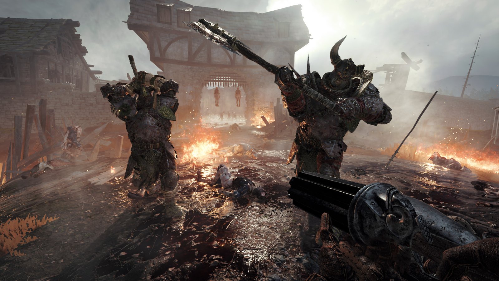 Two armoured Chaos Warriors advance through a burning village while the player aims a gun in Vermintide 2.